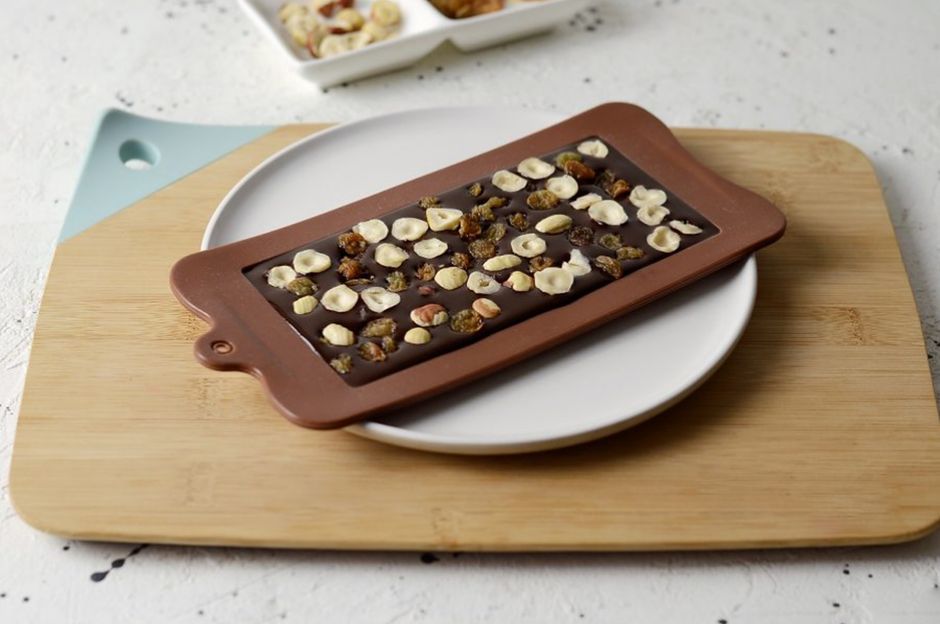Moule en silicone avec chocolat et morceaux de noisettes sur une planche en bois et une assiette blanche.