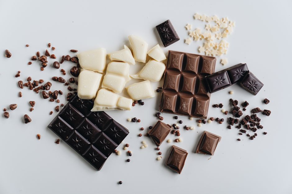 Différents types de chocolat et praliné disposés sur une surface blanche, incluant chocolat noir, au lait et blanc.