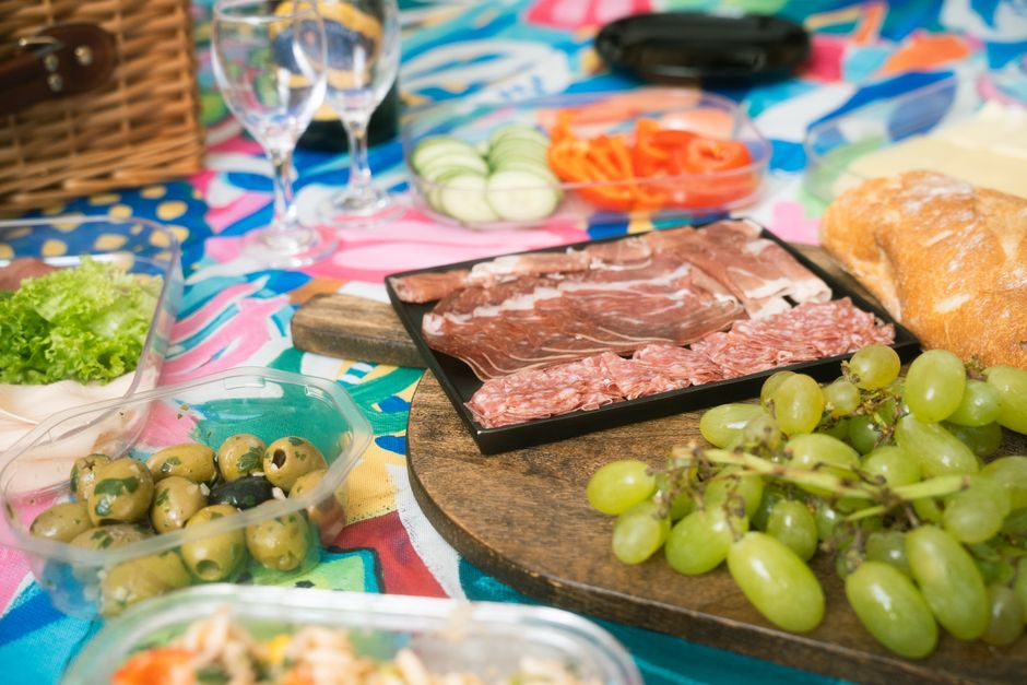 Plateau de charcuterie avec olives, raisins et légumes frais, sur une nappe colorée, pour une box gourmande.