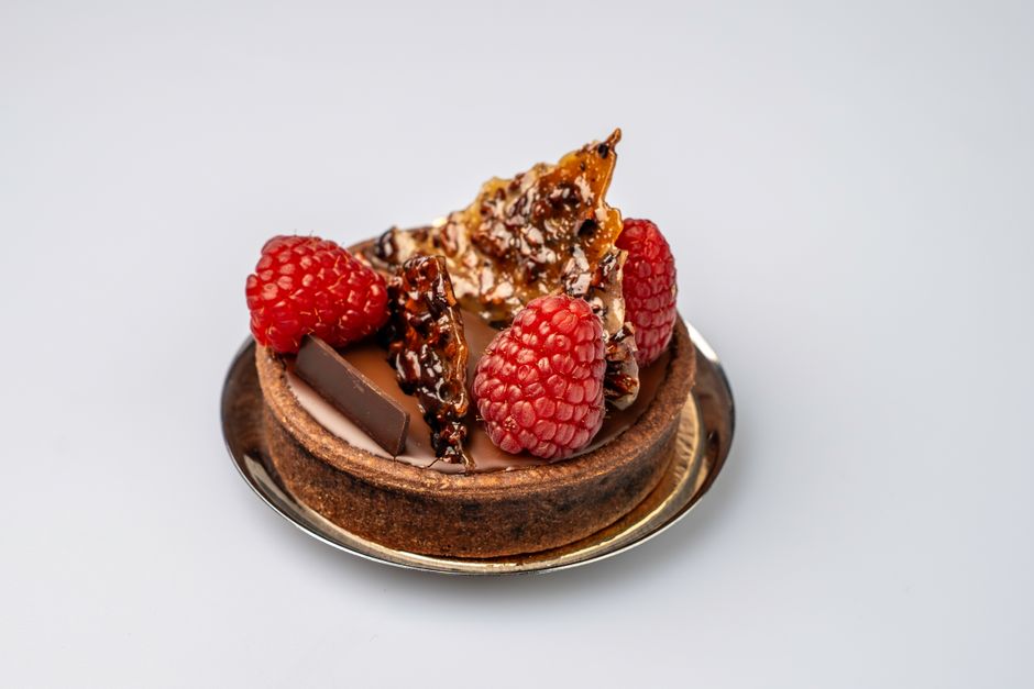 Tarte au praliné noisette décorée de framboises et de caramel croquant sur assiette argentée.