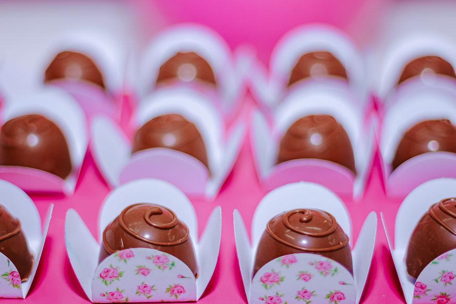 Truffes au chocolat présentées dans des caissettes blanches décorées de fleurs sur un fond rose.