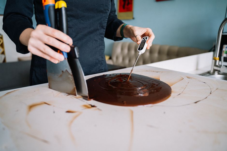 Personne utilisant une spatule et un thermomètre pour travailler du chocolat fondu sur un plan de travail.