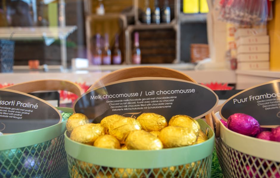 Des œufs en chocolat dorés et colorés dans une boîte élégante, entourés de décorations festives.