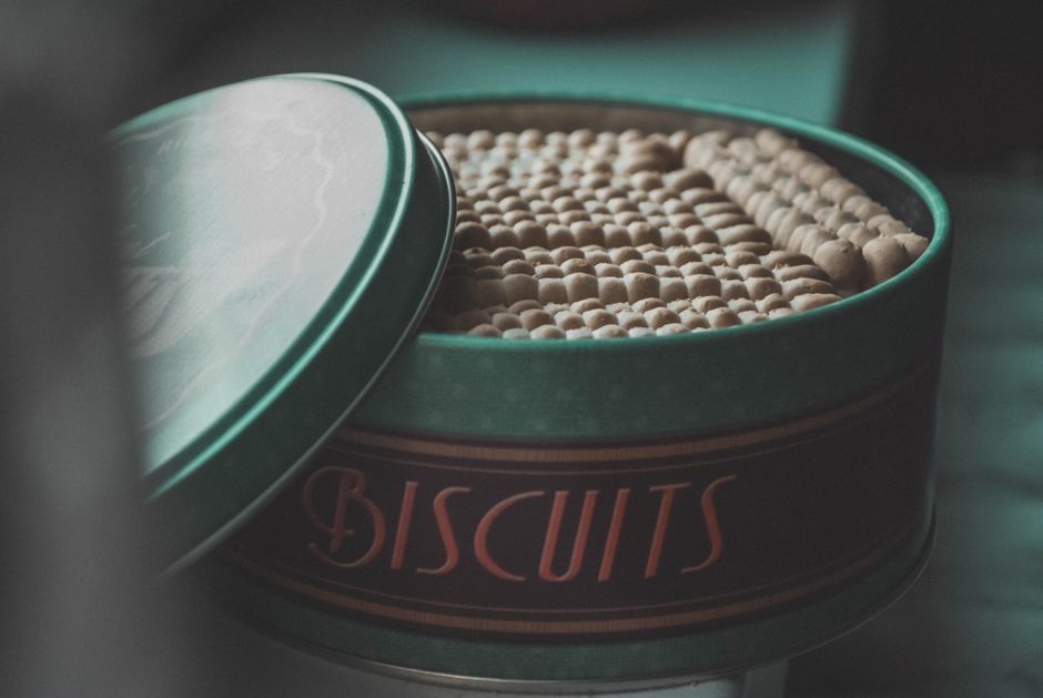 Boîte vintage de biscuits ouverte, révélant des biscuits en forme de petits ronds et de bâtonnets.
