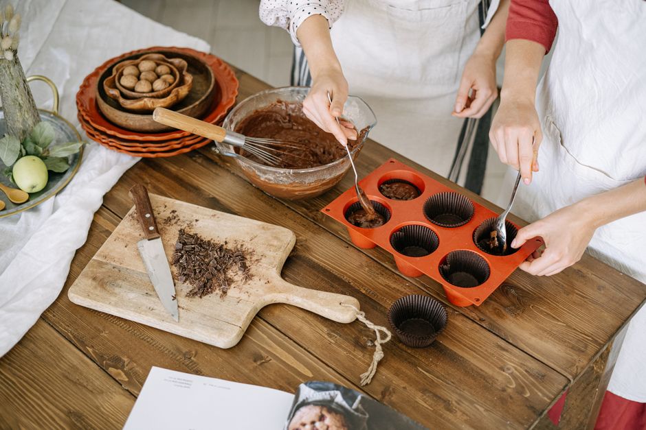 Préparation de coques en chocolat avec des mains utilisant des fouets dans un moule en silicone sur une table en bois.