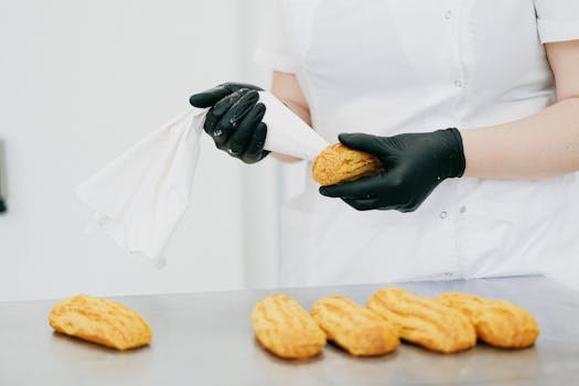 Pâtissier en train de garnir des éclairs avec une poche à douille dans une cuisine professionnelle.