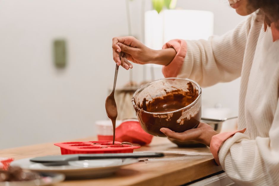 Femme versant du chocolat fondu dans un moule en silicone sur un plan de travail en bois.