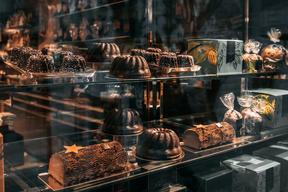 Vitrine d'une chocolaterie avec divers gâteaux et chocolats élégamment présentés sur des étagères.