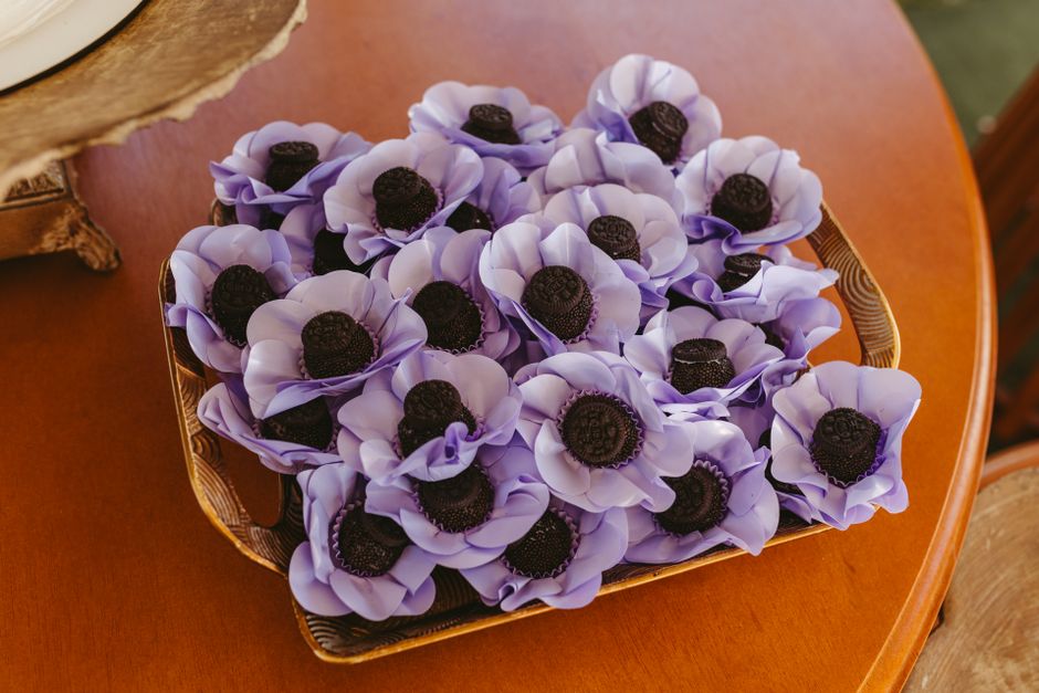 Plateau en bois avec des fleurs en sucre violettes et centres en chocolat, évoquant un mariage entre fleurs et chocolat.