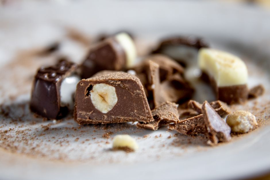 Praliné noisette maison en morceaux sur une assiette, avec des éclats de chocolat et des noisettes visibles.