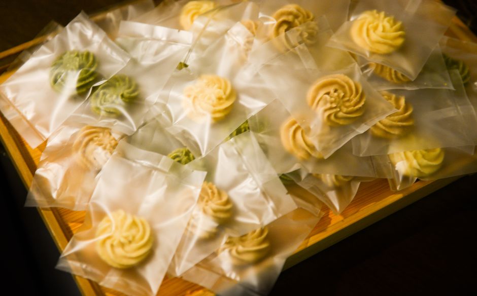 Petits biscuits en forme de spirale, emballés individuellement dans des sachets transparents sur un plateau en bois.